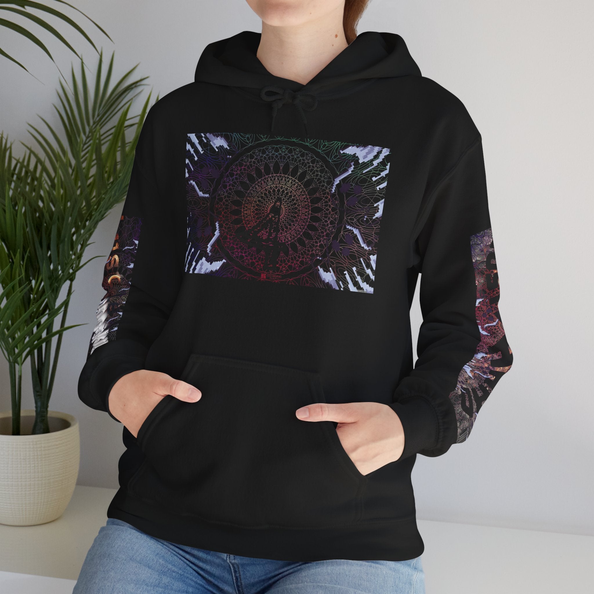 Person wearing a black hoodie with colorful designs, standing indoors next to a plant.